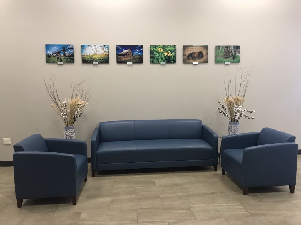 A blue couch and two chairs are arranged in front of a wall adorned with various pictures